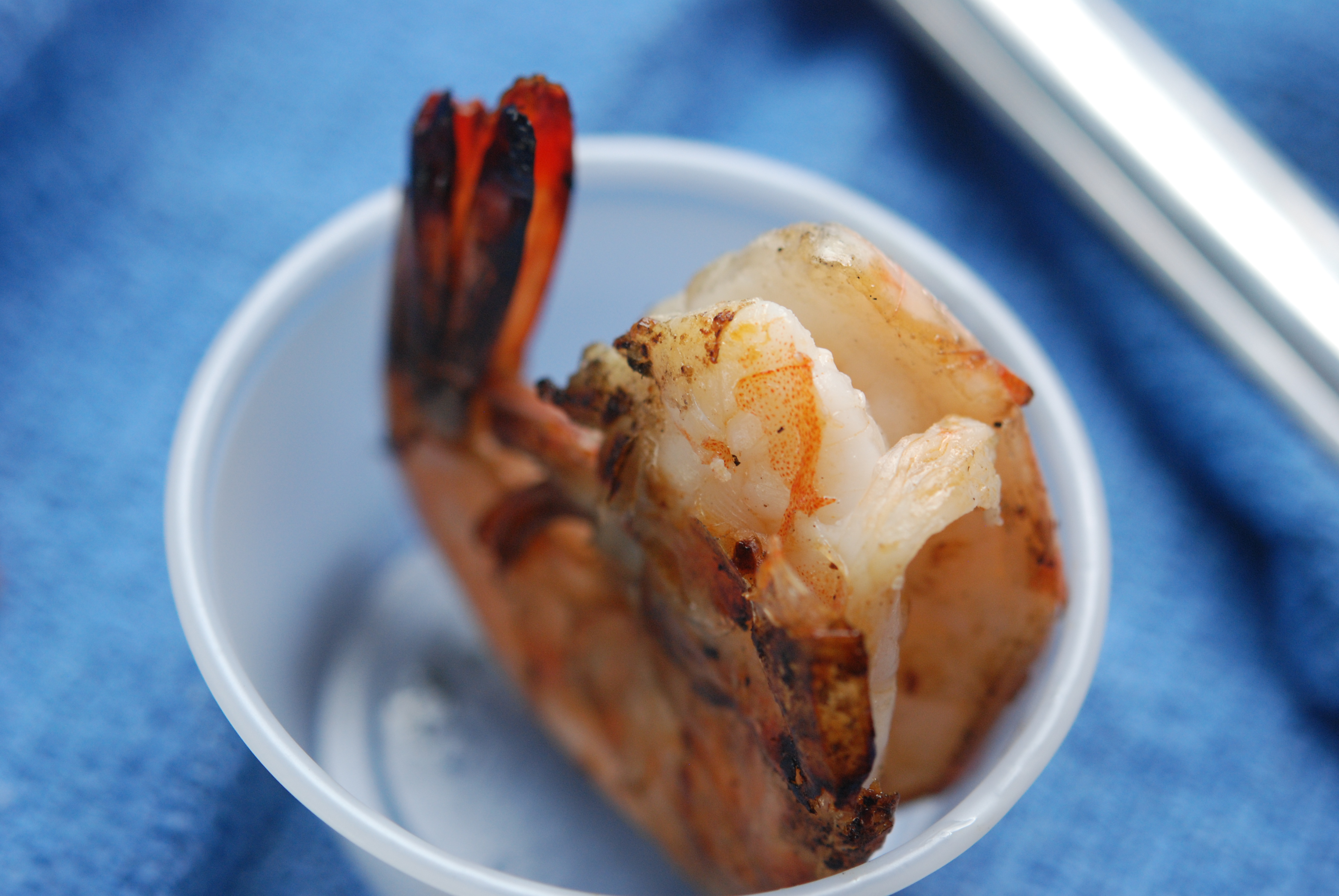 Cooked shrimp in plastic cup on blue cloth.