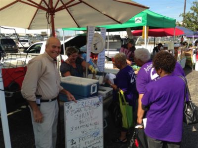 Seafood Sales Under Umbrella, Smiling Man, With Women In Purple T-shirts.