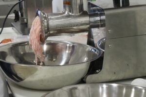 Ground fish coming out of a stainless steel meat grinder.